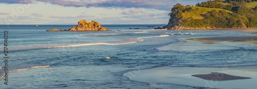 Quadro su tela Scenic coastal view of gentle ocean waves breaking on a sandy beach near rocky islets and green hills in Opoutere, Coromandel, New Zealand