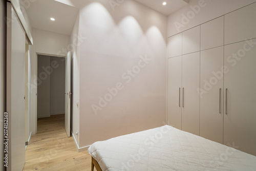Minimalist modern bedroom with white bed, light wood flooring, builtin wardrobes, and soft recessed lighting in calm contemporary residential interior, with bedroom, minimalist, modern, white detail