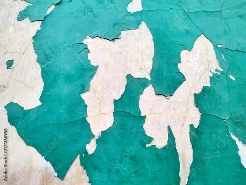 Close-up of cracked and peeling teal green paint layers on a weathered concrete wall, revealing rustic wall texture.