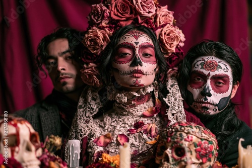 Young Latina woman with ornate Catrina skull makeup and rose crown, solemn and intimate for Day of the Dead remembrance with copy space