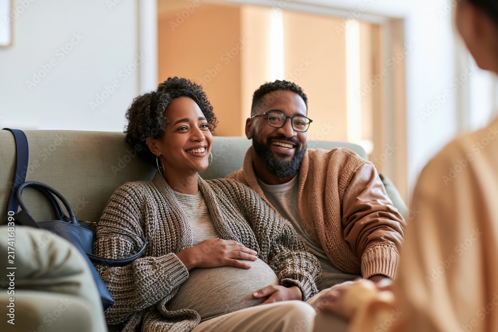 Fototapeta premium Pregnant woman and her partner sitting on a soft sage green sofa, smiling during a supportive prenatal counselling session for family wellness