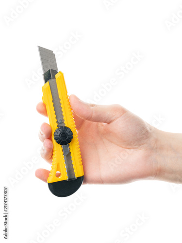 Fotografie A hand holding a yellow box cutter or utility knife, shown on a white background