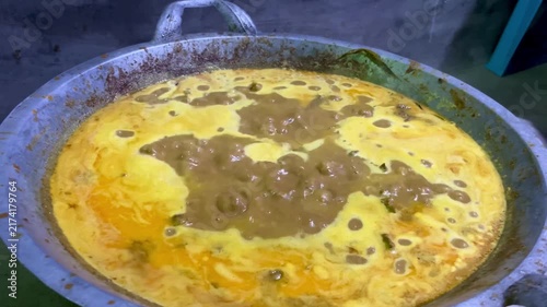 High angle shot of traditional Indonesian yellow curry gravy simmering in a large aluminum wok pan during cooking process