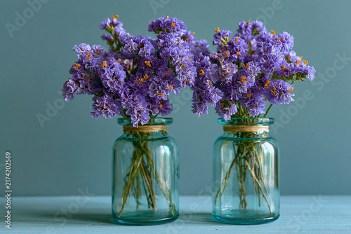 Two vintage glass jars filled with purple statice flowers on a rustic wooden table