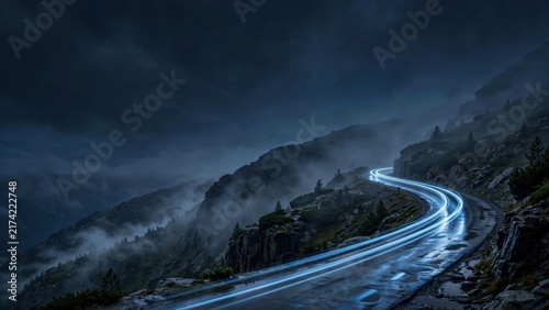 Winding mountain road with car light trails under a dark, misty, cloudy sky. Wet asphalt reflects