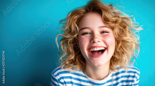 A cheerful girl with curly hair laughs joyfully against a vibrant blue background, exemplifying the essence of happiness and youthful exuberance in a playful setting.