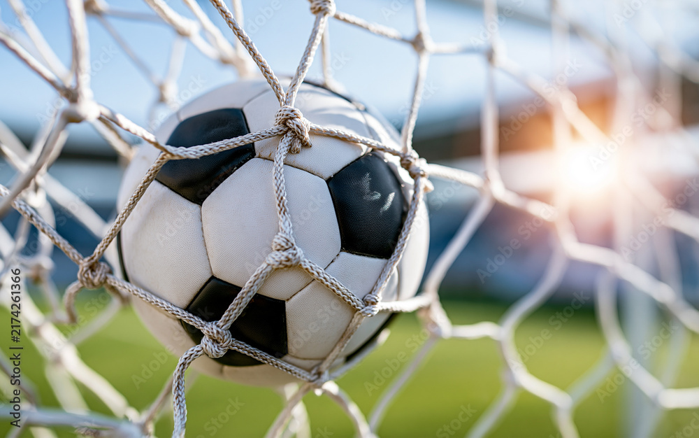 Naklejka premium Soccer ball hitting goal net on green field