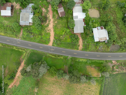 Obraz na plátně Aerial view of rural asphalt road passing green rice fields and farmhouses during rainy season