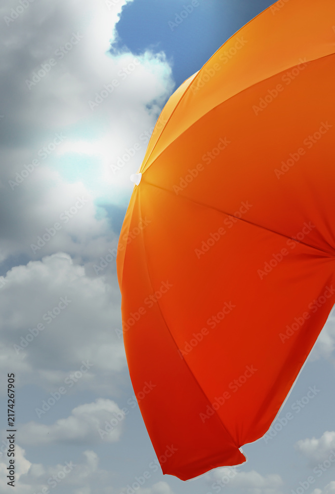 Obraz premium Orange sun umbrella against blue sky with fluffy clouds. Summer season