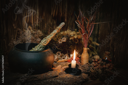 Foto Mystical autumn witchy altar with steaming iron cauldron, dried herbs, burning candle and magic tools