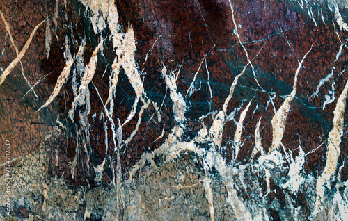 Closeup of polished marble with brown, teal, white, and cream mineral veins forming an intricate natural stone texture.