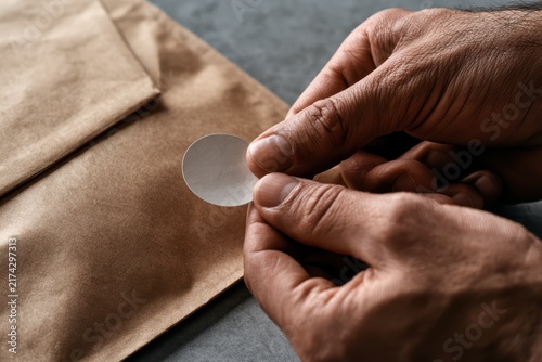 Hands Applying Circular Sticker to Package for Gift Wrapping or Labeling