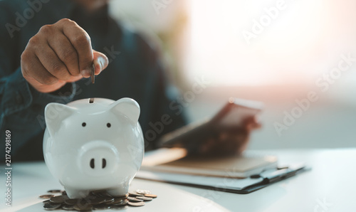 Close-up Hand putting coins into a white piggy bank saving bank for account save money. Planning step up, saving money for future plan, retirement fund. Business investment-finance accounting concept.