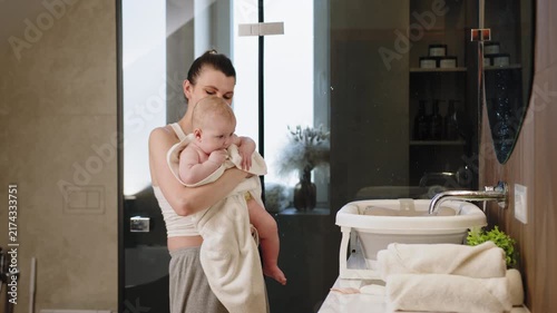 Woman tenderly embraces infant wrapped in soft towel sharing a joyful moment indoors. A mother tenderly holds infant showing care love and gentle family bonding