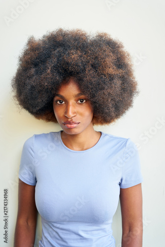 Woman With Big Curly Hair Stands in Front of a Plain Wall