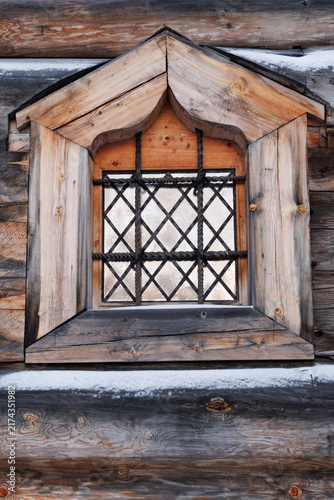 Quadro su tela Traditional carved wooden frame and iron grate of an old window on log wall of the Intercession Church in winter Zaostrovie, Russia