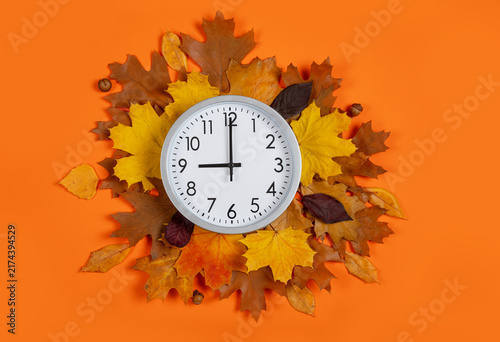 9 o'clock, round wall clock on autumn leaves wreath over orange background, daylight saving time concept. Conceptual flat lay composition for transition of the fall season, time management, fall sales