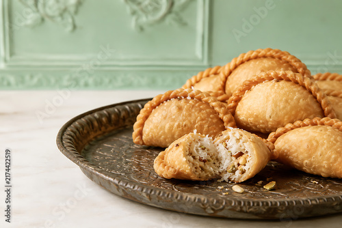 Gujarati ghughra pastries with finely crimped crescent edges, one broken open showing coconut and nut filling, antique embossed tin tray