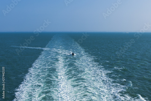 Fotografie small motorboat traveling wide white water wake left behind large ship