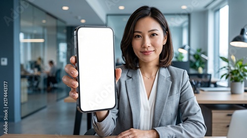 Asian businesswoman holding a smartphone with a blank white screen in a modern office environment