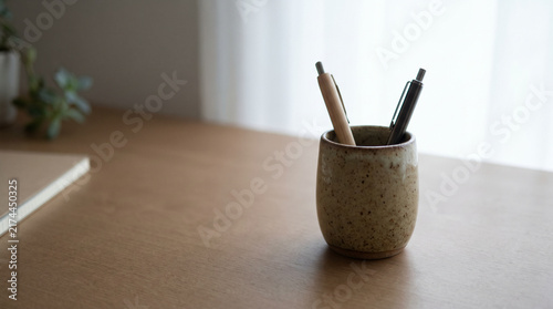 Minimalist wooden desk setup with ceramic pen holder and stationery by window with copy space