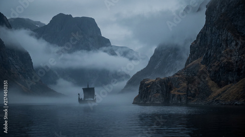 Viking longship sailing through misty dark fjord between dramatic rocky mountains with copy space