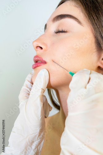Beautiful young woman receiving a lip filler injection from a doctor in black gloves, cosmetic beauty treatment, facial aesthetic procedure, clinic wellness.