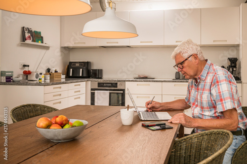 Senior man working in the kitchen on a laptop
