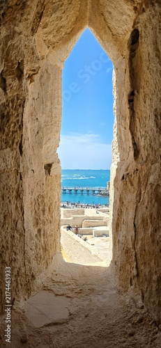 View of the Mediterranean Sea through an ancient stone window in the Qaitbay Citadel, a 15th-century defensive fortress located on the Mediterranean coast, on Pharos Island in Alexandria, Egypt.
