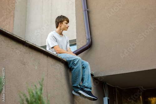 A teenager going through a difficult time sits on the edge of a roof, his posture conveying stress and anxiety, a conceptual image of the emotional turmoil and struggles during adolescence
