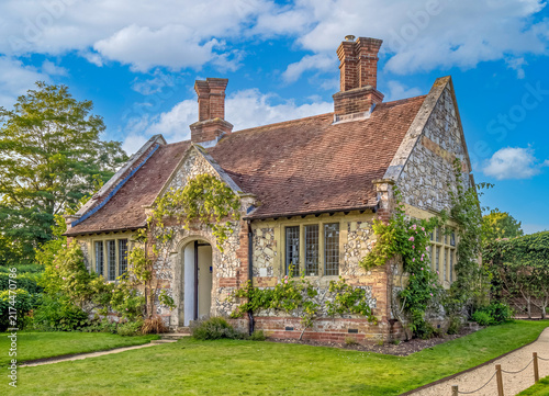 Ein charmantes, altes Landhaus aus Naturstein und Backstein mit Kletterpflanzen, umgeben von einem grünen Garten an einem sonnigen Sommertag in Hampshire.