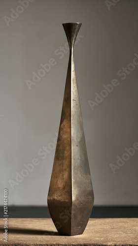Bronze vase featuring a slender elongated silhouette rests gracefully upon a wooden surface.