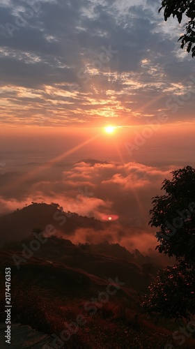 Sunset over a sea of clouds covering rolling hills with warm orange and pink hues painting the dramatic evening sky.