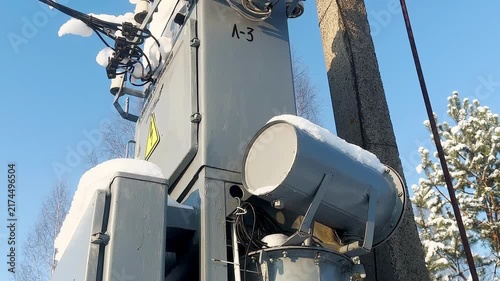 A snow-covered outdoor electrical transformer installed next to a concrete power line pole in a rural area.