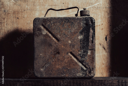 Vintage rusty metal jerrycan on dark rustic wooden background, closeup. Old scratched and rusty fuel canister stands on textured wood surface with dramatic lighting and dark shadows