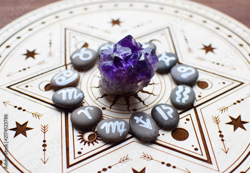 Foto Natural amethyst crystals and stones bearing the emblems of the zodiac signs are arranged on a wooden altar for divination