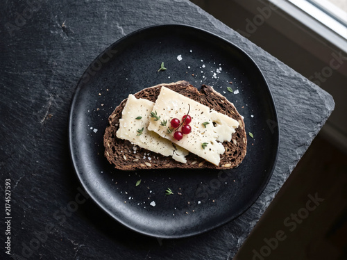 Dark rye black bread slice topped with cheese served on black ceramic plate gourmet appetizer
