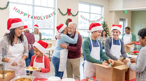 Holiday Cheer and Giving Hands: A warm scene of community spirit unfolds as diverse volunteers, adorned in festive Santa hats and aprons, prepare and distribute holiday meals.