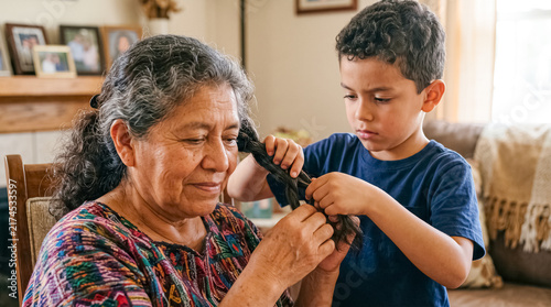 Grandchild braiding grandmother's hair: A young boy attentively braids his grandmother's long dark hair, showing care and affection in a heartwarming domestic scene.