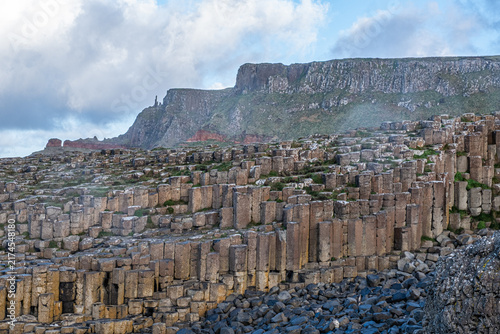Foto Terraced layers of volcanic basalt columns rising toward high coastal cliffs at