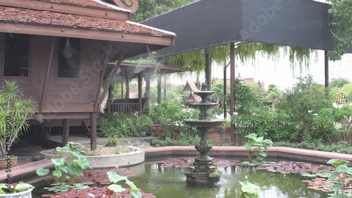 scenic garden landscape featuring a multi tiered fountain in a water lily pond with cooling water mist sprays beside an authentic oriental wooden pavilion house