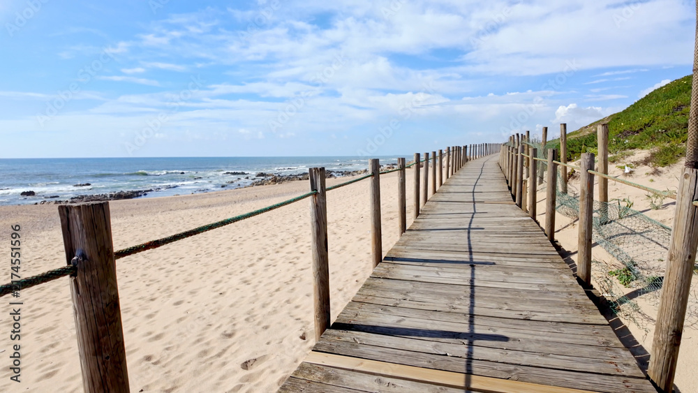 Fototapeta premium Wooden Boardwalk Leading Along the Sandy Coastline of Miramar Beach in Portugal