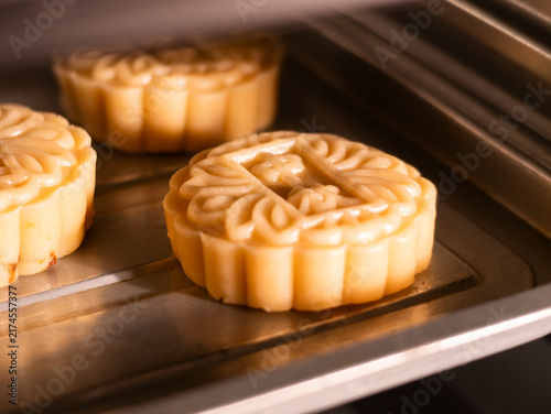 Traditional Chinese Mid‑Autumn Festival, handmade Cantonese mooncakes. Hands brush egg liquid on raw mooncake pastries, mooncakes placed on baking tray. Traditional festival food baking, folk custom, 