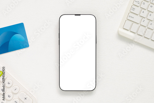 Top view smartphone mockup with blank white screen, blue payment card, keyboard and calculator on white desk. Concept for mobile banking, finance, e commerce, digital payment, app presentation.