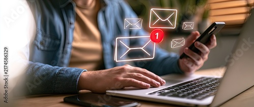 Person using laptop and smartphone with email notifications appearing.