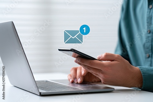 Person checking smartphone for new email notification while using laptop.