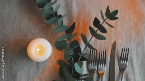 Dining table setup featuring glowing candle and silver cutlery with motion video clip of greenery