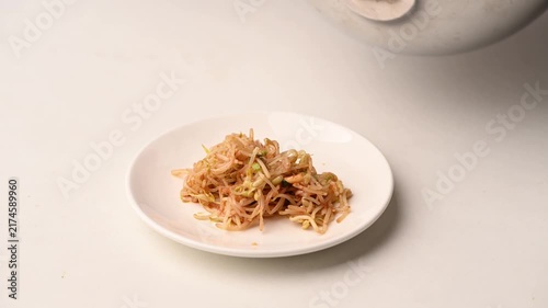 Hands placing Korean bean sprout salad (Kongnamul Muchim) onto a white plate