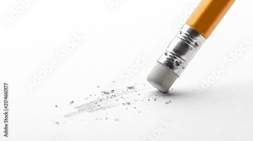 macro close-up of a classic yellow wooden pencil with a silver metal ferrule and soft gray rubber eraser actively erasing graphite marks from a clean white paper surface, tiny eraser 