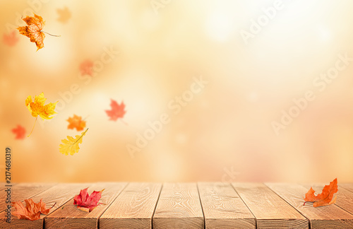 Autumn nature background with falling leaves and a wooden table. Background for educational, Thanksgiving, or Harvest Day themes.